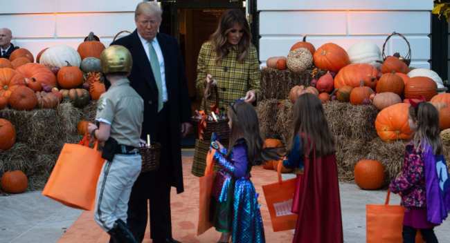 Президент США Дональд Трамп и первая леди Мелания Трамп раздают детям конфеты на праздновании Хэллоуина в Белом доме в Вашингтоне. 28 октября 2018 года
